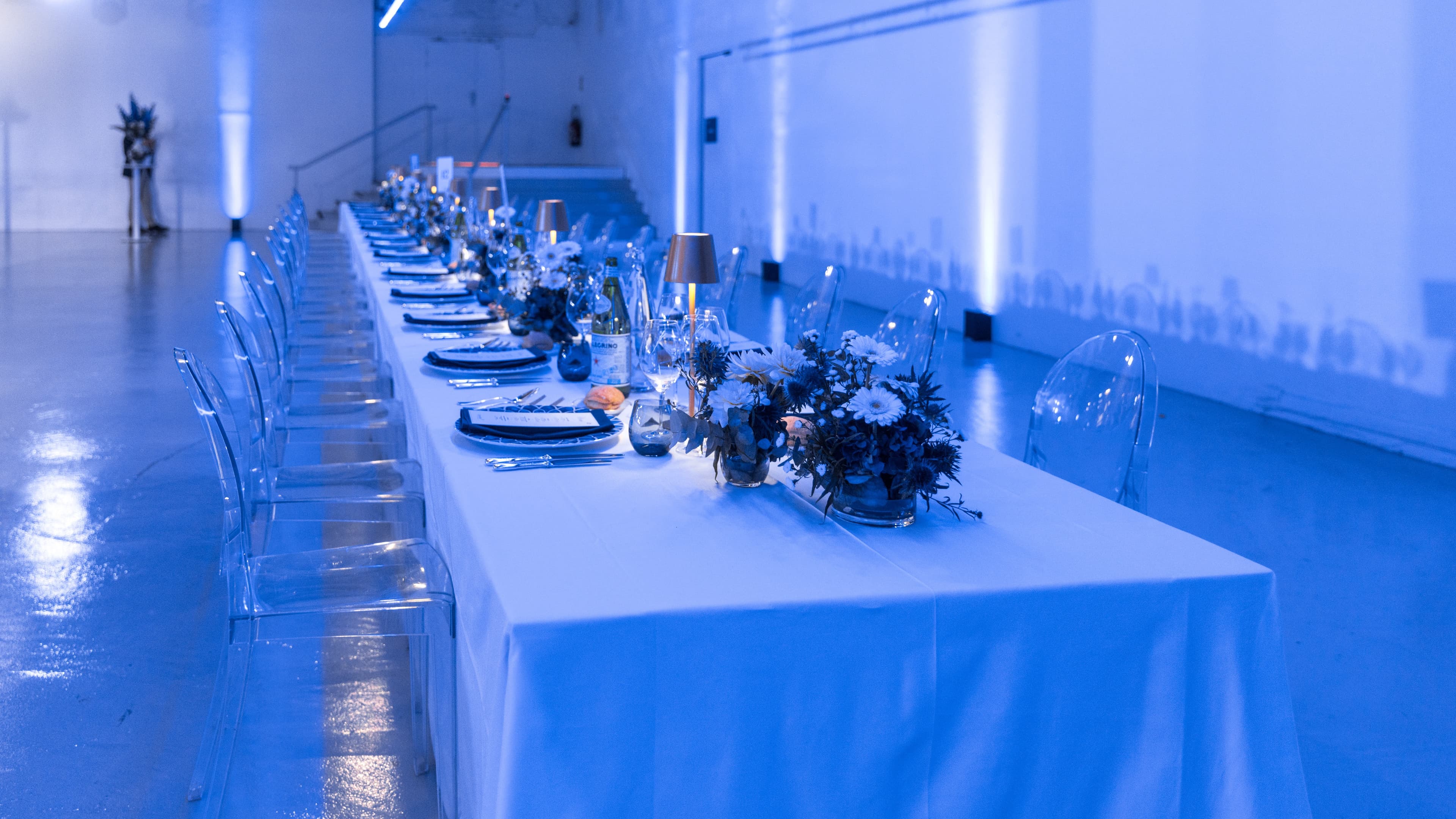 Grande table de dîner sous lumière bleue, compositions florales et lampes dorées, pour l'Investor Day Quilvest au Palais de Tokyo