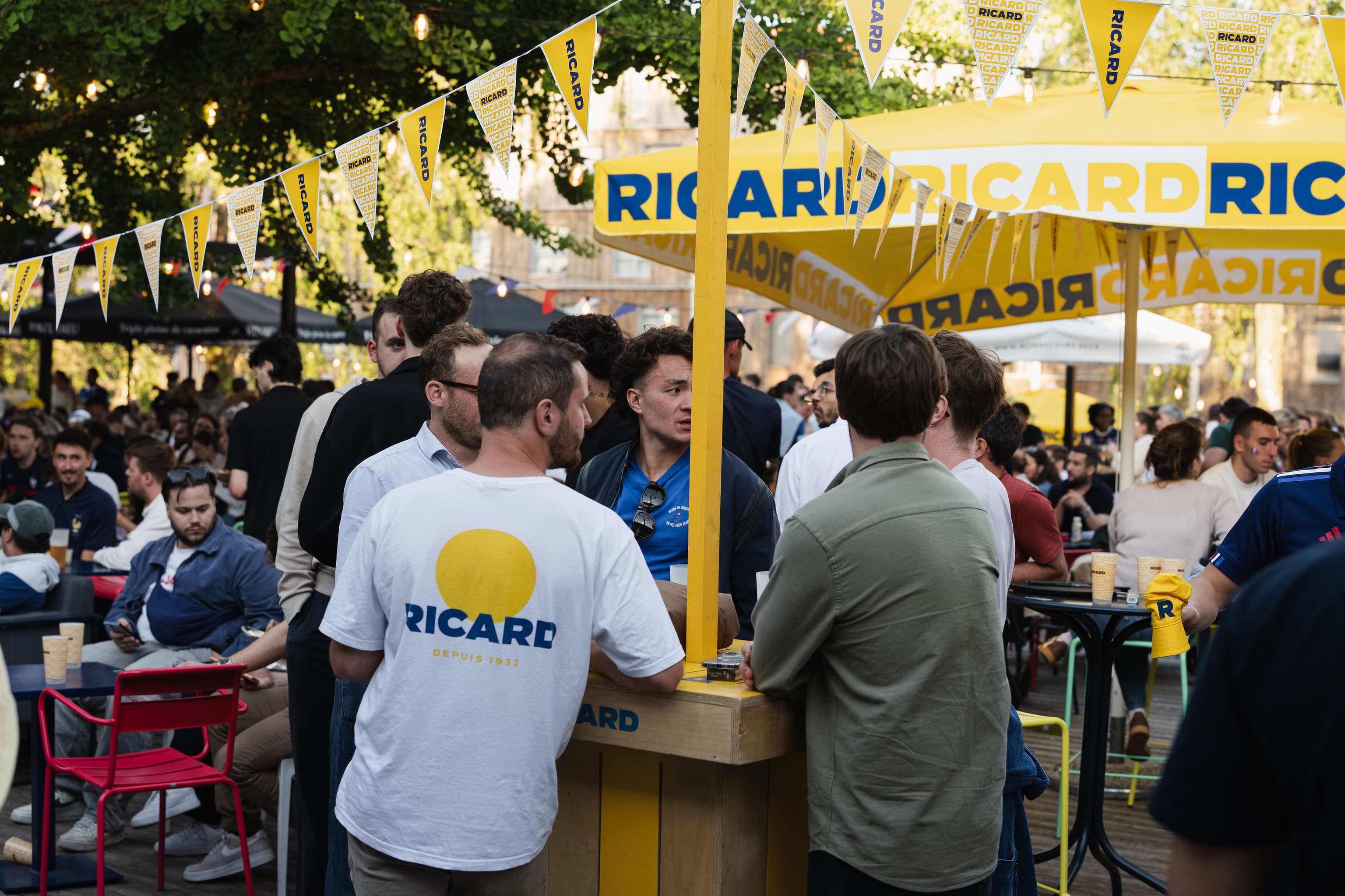 Public rassemblé au comptoir Ricard sous les parasols et fanions lors d'une étape urbaine de la tournée